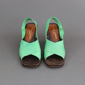 May include: A pair of green heeled sandals with a criss-cross strap design. The sandals have a brown leather sole and are labeled "Pierre Cardin Paris".