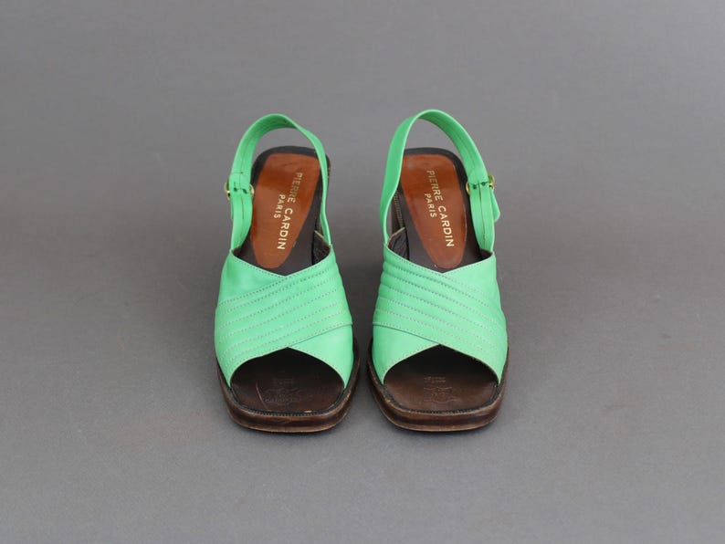 May include: A pair of green heeled sandals with a criss-cross strap design. The sandals have a brown leather sole and are labeled "Pierre Cardin Paris".