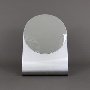 May include: A silver-coloured, freestanding tabletop mirror with a round, reflective surface.