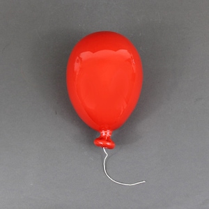 May include: A glossy red balloon-shaped object with a small red base and a white string. The balloon is centered on a gray background. The object is likely a decorative item or a toy.