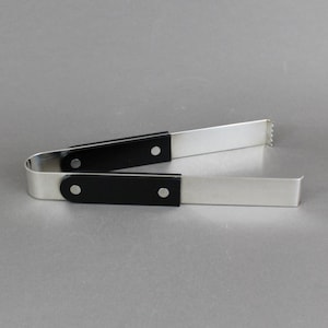 May include: Silver ice tongs with black handles. The tongs have a U-shaped design with a serrated edge on one end. The black handles are attached with rivets. The tongs are designed for serving ice.