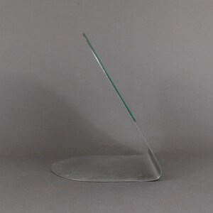 May include: A clear glass picture frame with a silver base. The frame is angled and has a curved base.