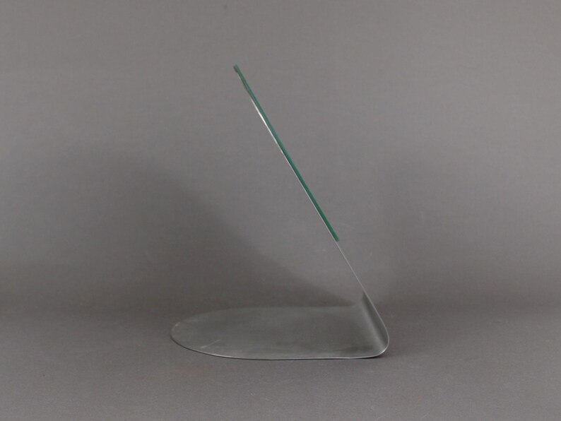 May include: A clear glass picture frame with a silver base. The frame is angled and has a curved base.