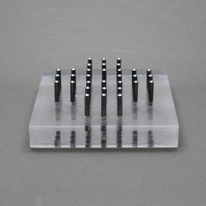 Peut inclure: Un bloc rectangulaire en acrylique transparent doté d'une grille de vingt-cinq tiges cylindriques noires verticales disposées en cinq rangées et cinq colonnes. Chaque tige possède un petit sommet circulaire argenté et réfléchissant.