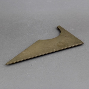 May include: A bronze-colored, triangular metal object with a curved section on one side. The object has a flat, matte finish and appears to be a component or part of a larger item. The shape is geometric and the overall design is simple.