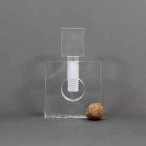 May include: A clear acrylic nutcracker with a white screw and a brown walnut next to it.