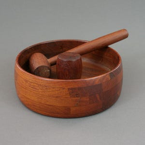 May include: A wooden nutcracker set with a bowl and two mallets. The bowl is made of dark wood with a patterned design. The mallets are also made of dark wood.