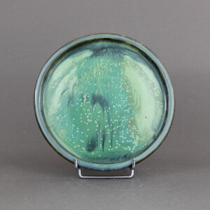 May include: A round ceramic plate with a green and white glaze. The glaze has a marbled effect with white speckles.