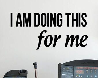 May include: A white wall with black text that reads "I AM DOING THIS for me". There is a black elliptical machine in the background.
