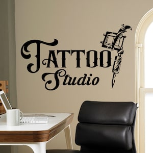 May include: Black and white tattoo studio sign with a stylized tattoo machine and the text "Tattoo Studio".