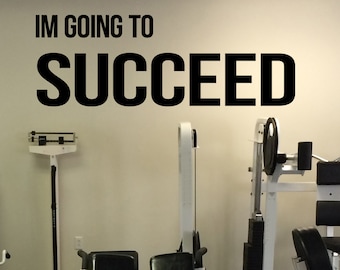 May include: A white wall with the text "IM GOING TO SUCCEED" in black lettering. The wall is in a gym with various exercise equipment, including a scale, a weight machine, and a back extension machine.