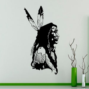 Può includere: Un adesivo murale in bianco e nero raffigurante il profilo di un nativo americano con lunghi capelli e due piume. Il design è una silhouette, con un lavoro di linea dettagliato sui vestiti e sul viso.