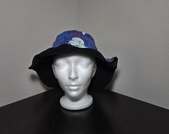 May include: A blue and black bucket hat with a white and black graphic print. The hat has a black brim and a black band around the crown.