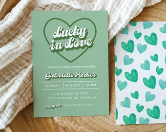 May include: A green and white bridal shower invitation with the text "Lucky in Love" in a heart shape. The invitation includes the name Gabrielle Parker, the date 04.06.2022, and the time 4 PM. The invitation also includes the location, The Garden Bistro, 11201 Ed Brown Rd, Charlotte. The RSVP information is included at the bottom of the invitation.