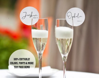 May include: Two champagne flutes with white table cards on top. The table cards are round and white with black text. The text on the table cards reads "Joshua Table 2" and "Ophelia Table 5".