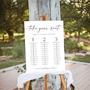 Könnte beinhalten: Eine weiße Sitzordnung mit schwarzem Text auf einer Holzstaffelei. Der Text lautet "take your seat" und listet Namen unter den Nummern 1, 2 und 3 auf. Das Datum "09.20.20XX" wird ebenfalls angezeigt. Unten steht "we're so glad you're here!"