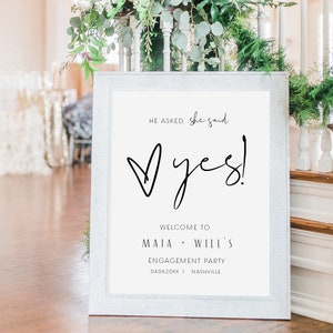 May include: A white sign with black text announcing an engagement party for Maia and Will. The sign reads "He asked, she said, Yes!" with a heart shape and the date "04.06.20XX" and location "Nashville".