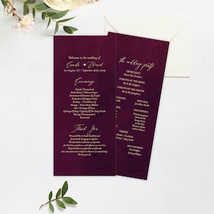 May include: A burgundy wedding program with gold lettering. The program includes the ceremony order, the wedding party, and a thank you message from the couple. The text reads "Welcome to the wedding of" and "The wedding party".