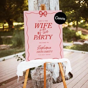 以下が含まれることがあります： 木製のイーゼルに立てられたピンク色の看板。赤い文字で「SHE'S THE WIFE of the PARTY」と書かれています。その下に「WELCOME TO stephanie HENS PARTY!」と日付と場所が書かれています。Canvaのロゴが右上隅にあります。