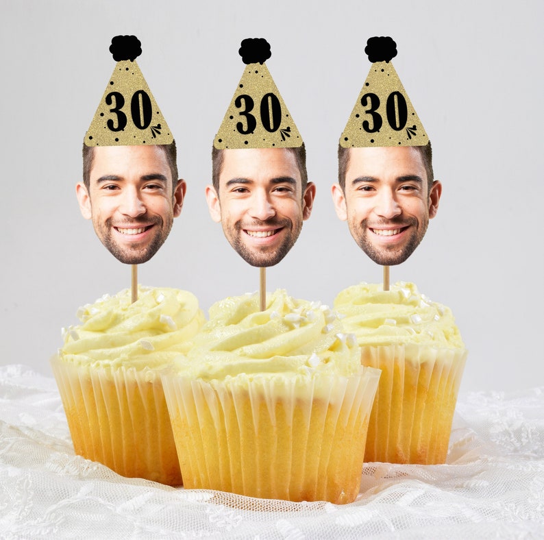 May include: Three cupcakes with white frosting and sprinkles topped with a gold glitter party hat with a black pom-pom and the number "30" in black. Each hat has a face cutout with a smiling man's face.