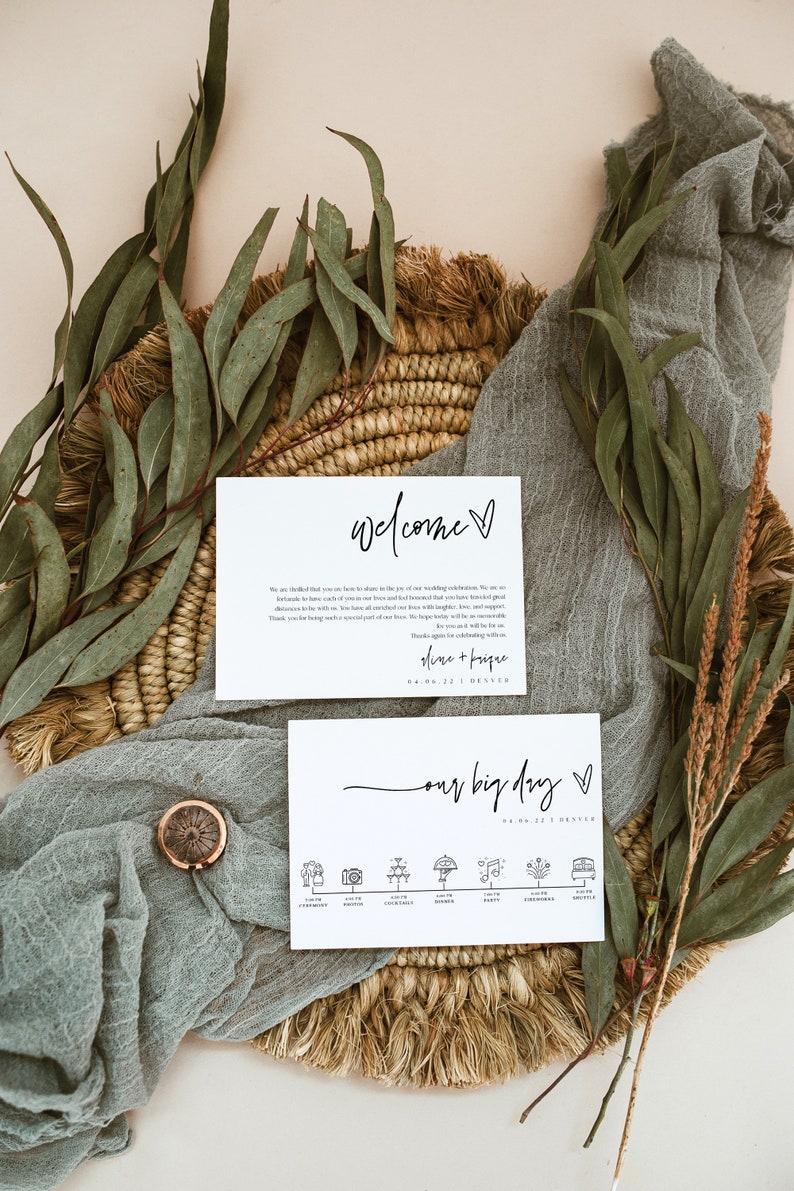 May include: A wedding welcome sign with the text "Welcome" and "Our Big Day" with a heart symbol. The sign also includes the date "04.06.22" and the location "Denver". The sign is on a woven basket with green eucalyptus leaves and a light blue fabric.