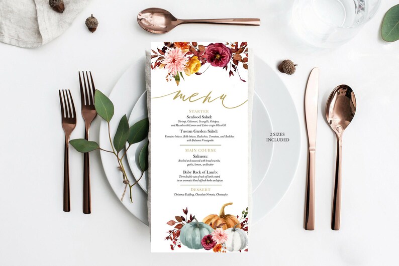 May include: A menu card with a floral design and the word "menu" in gold script. The menu features a fall theme with pumpkins and flowers. The card is placed on a white plate with copper-colored cutlery.