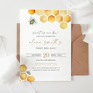 May include: A white invitation card with gold lettering and a watercolor illustration of a honeycomb and a bee. The text reads "Sweet as can bee! Join us in celebrating Alana Smith's First Bee-Day! Saturday, April 20, 2021 at 4:00 in the afternoon. The Henderson Residence, 123 Main Street, Dallas, TX 399. RSVP to Alana at 333-444-555 by April 1st. Registered at Target and Amazon.com"