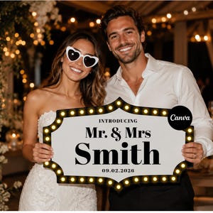 Könnte beinhalten: Ein rechteckiges Schild im Festzelt-Stil mit abgerundeten Kanten und beleuchteten gelben Glühbirnen am Rand. Das weiße Schild trägt den schwarzen Text: INTRODUCING Mr. & Mrs Smith 09.02.2026. Das Schild wird von zwei Personen in festlicher Kleidung gehalten.