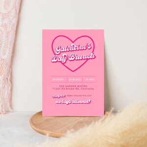 May include: Pink invitation card with a heart-shaped outline and the text "Galentine's Day Brunch" in a retro font. The card includes details for the event, including the date, time, location, and RSVP information. The text "no boy's allowed!" is also included.