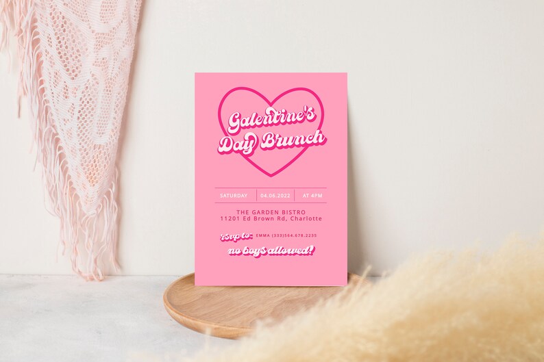 May include: Pink invitation card with a heart-shaped outline and the text "Galentine's Day Brunch" in a retro font. The card includes details for the event, including the date, time, location, and RSVP information. The text "no boy's allowed!" is also included.