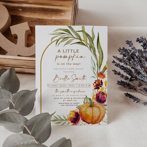Pu&ograve; includere: Invito per baby shower con design floreale e zucca ad acquerello. L'invito presenta il testo "A Little Pumpkin is on the way!" con il nome, la data e l'ora dell'invitato d'onore. Il design include foglie verdi, fiori arancioni e viola.