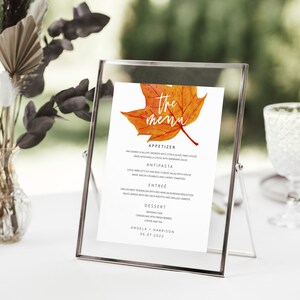 May include: A printable wedding menu with a watercolor illustration of an orange and red maple leaf. The text reads "The Menu" and includes the names Angela and Harrison and the date 08.07.2022.