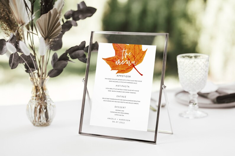May include: A printable wedding menu with a watercolor illustration of an orange and red maple leaf. The text reads "The Menu" and includes the names Angela and Harrison and the date 08.07.2022.