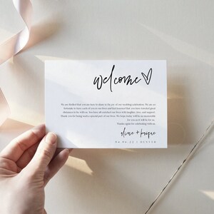 May include: A white welcome sign with black calligraphy that reads "welcome" with a small heart. The text below reads "We are thrilled that you are here to share in the joy of our wedding celebration. We are so fortunate to have each of you in our lives and feel blessed that you have traveled great distances to be with us. We have cherished all our time with you, your laughter, and support. Thank you for being such a special part of our lives. We hope today will be an unforgettable celebration. Thank you again for celebrating with us.  Alana +  Bosque 08.06.22 | Denver"