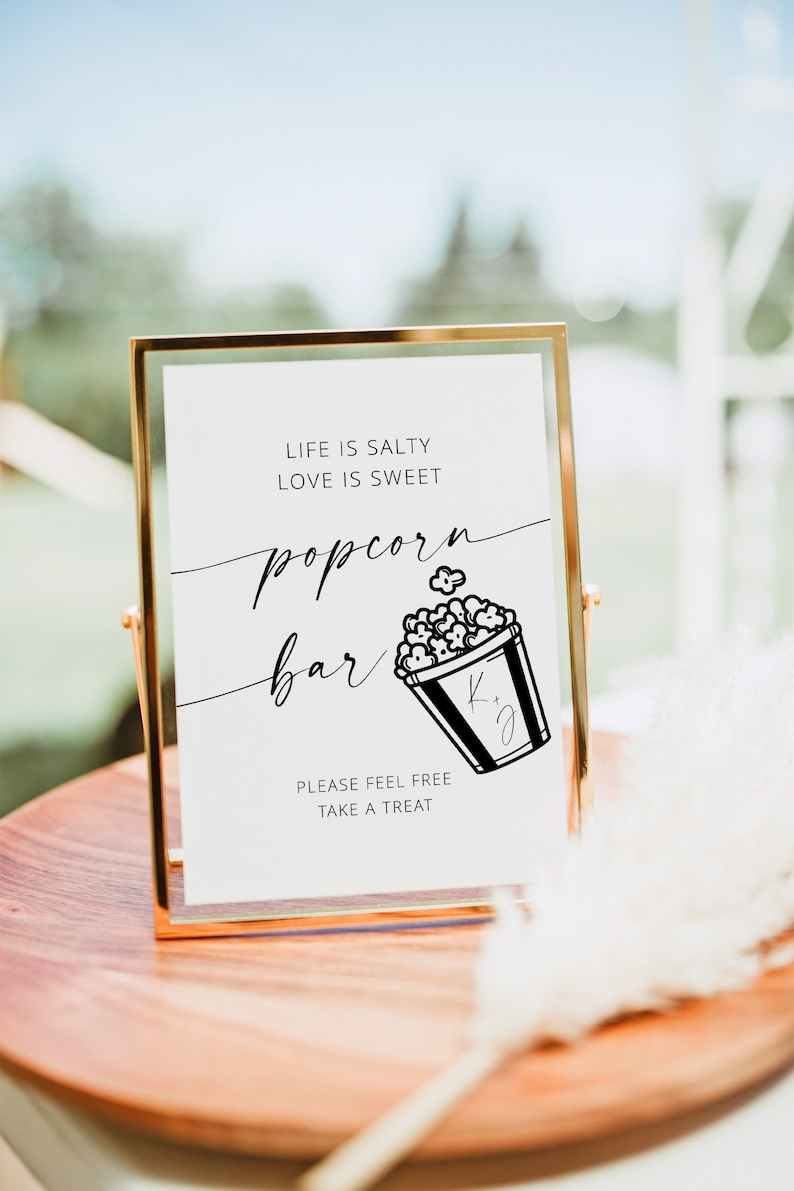 May include: A gold framed sign with the text "Life is salty, love is sweet, popcorn bar" with a black and white illustration of a popcorn bucket. The sign also says "Please feel free, take a treat."
