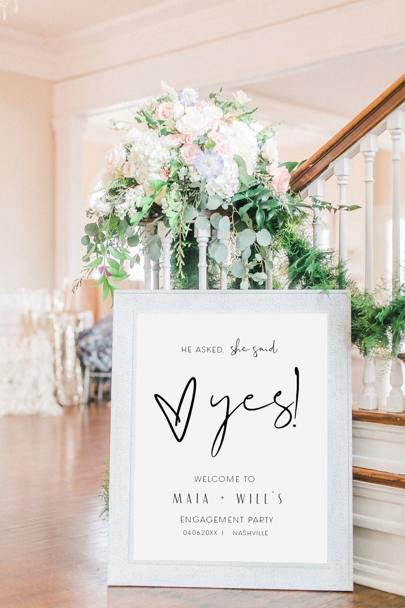 May include: A white sign with black text announcing an engagement party for Maia and Will. The sign reads "He asked, she said, Yes!" with a heart shape and the date "04.06.20XX" and location "Nashville".