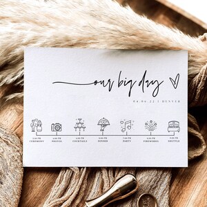 May include: A white card with the text "our big day" in black cursive script. The date "04.06.22" and the location "DENVER" are printed below the text. A timeline of events for the day is listed below, with icons representing each event. The icons include a couple, a camera, champagne glasses, a dinner plate, a musical note, fireworks, and a bed.