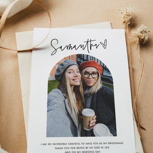 May include: A white card with a photo of two women smiling at the camera. The card has the text "Samantha" with a heart symbol and the message "I am so incredibly grateful to have you as my bridesmaid. Thank you for being by my side in life and on my wedding day."