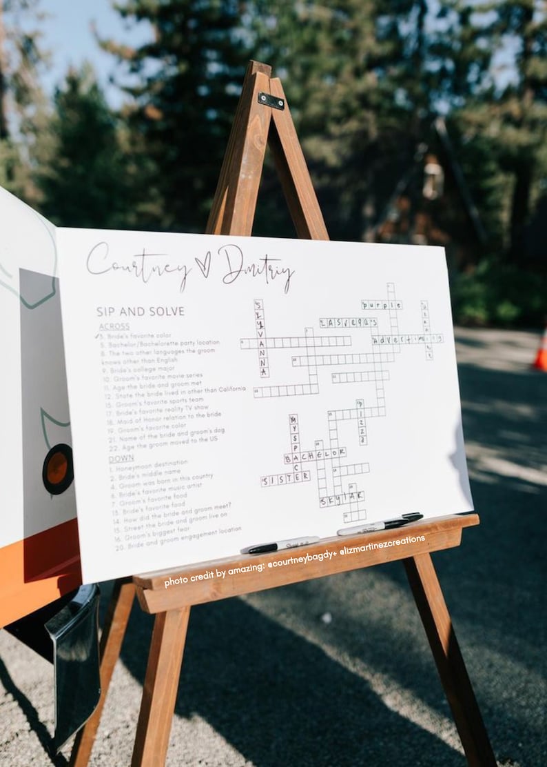 May include: A white crossword puzzle on an easel with the title "Courtney & Dmitry Sip and Solve". The crossword puzzle has clues about the couple's relationship and wedding.