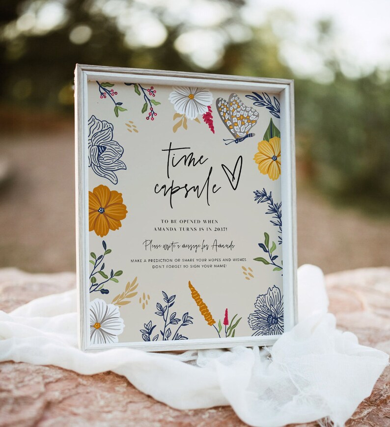Puede incluir: Un cartel enmarcado en blanco con un dise&ntilde;o floral y el texto "time capsule" con un coraz&oacute;n. El cartel pide a los invitados que escriban un mensaje para Amanda que se abrir&aacute; en 2037.