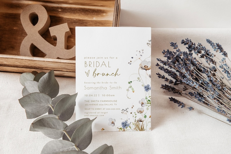 May include: A white invitation card with a floral design and gold lettering. The text reads "Please join us for a Bridal Brunch honoring the bride-to-be Samantha Smith 10.04.22 | 10:00am The Smith Farmhouse 123 Avenue 1234 Dallas, TX RSVP to Emmy at 000 000.000 registered at Target and Amazon.com"