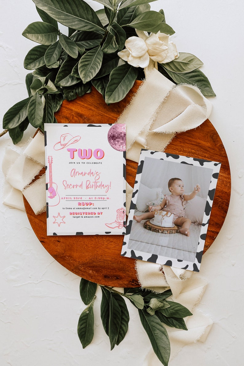 May include: A pink and white birthday invitation with a cow print border. The invitation says "Two" in pink letters and "Amanda's Second Birthday!" in pink and white letters. The invitation also includes a guitar, a cowboy hat, a star, and a cowboy boot. The invitation is on a wooden surface with a white ribbon and green leaves.