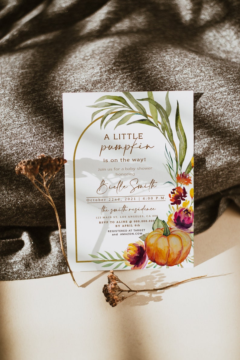 Pu&ograve; includere: Invito per baby shower con zucca e design floreale ad acquerello. Il testo recita "A Little Pumpkin is on the way!" con i dettagli dell'evento. Include una cornice dorata e elementi decorativi.