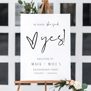 May include: White sign with black text announcing an engagement party for Maia and Will. The sign reads "He asked, she said yes!" with a heart and the date "04.06.20XX" and location "Nashville".