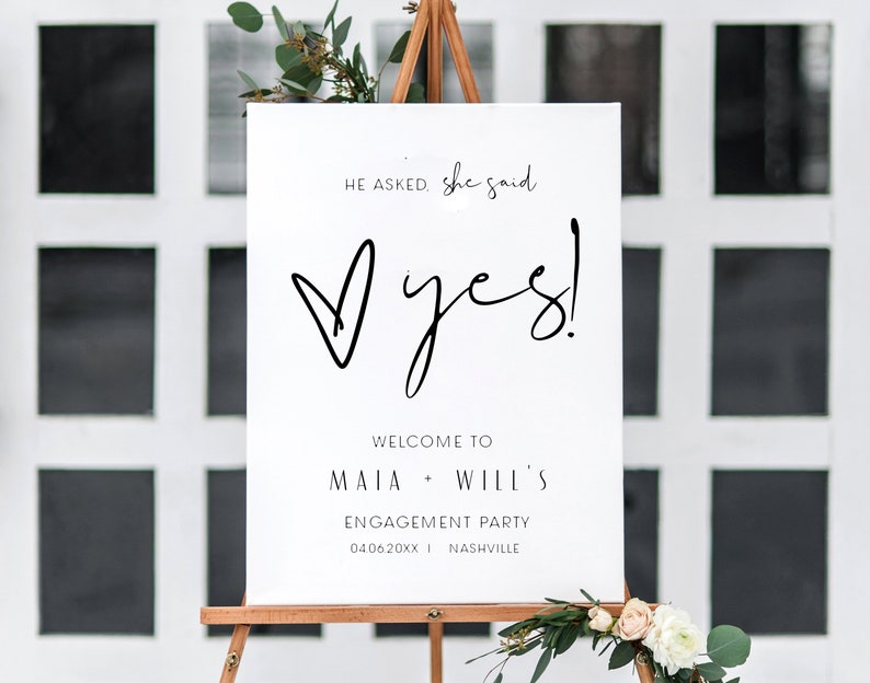 May include: White sign with black text announcing an engagement party for Maia and Will. The sign reads "He asked, she said yes!" with a heart and the date "04.06.20XX" and location "Nashville".