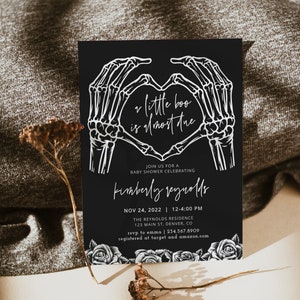 May include: Black and white baby shower invitation with a skeleton hand heart design. The text reads "a little boo is almost due" and includes the date, time, location, and RSVP information.