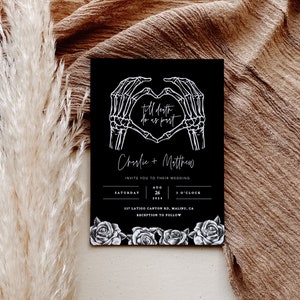 May include: Black wedding invitation with white skeleton hands forming a heart with the text "till death do us part" and the couple's names "Charlie + Matthew". The invitation includes the date, time, and location of the wedding.