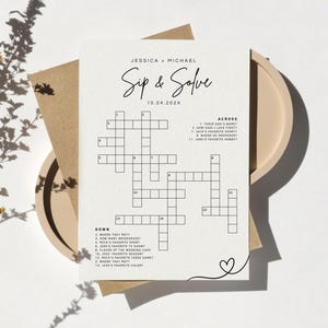 May include: A wedding-themed crossword puzzle card with the text "Sip & Solve" and the names Jessica and Michael. The card is on a beige plate with a brown envelope and a sprig of dried flowers.