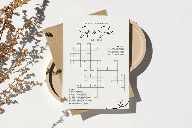 May include: A wedding-themed crossword puzzle card with the text "Sip & Solve" and the names Jessica and Michael. The card is on a beige plate with a brown envelope and a sprig of dried flowers.