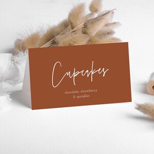 May include: A brown card with white text that reads "Cupcakes" with the flavors "chocolate, strawberry & sprinkles" listed below.